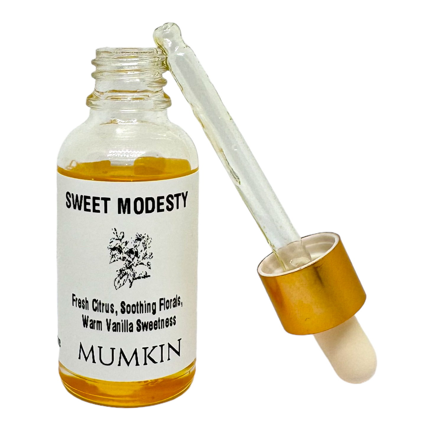 A close-up image of a "Sweet Modesty" fragrance oil bottle by Mumkin. The glass bottle contains golden-hued oil and has a white label with black text, listing its fragrance notes: "Fresh Citrus, Soothing Florals, Warm Vanilla Sweetness." A botanical illustration is featured on the label. The gold-capped dropper is resting beside the bottle, partially filled with oil, with a white rubber tip. The background is plain white.