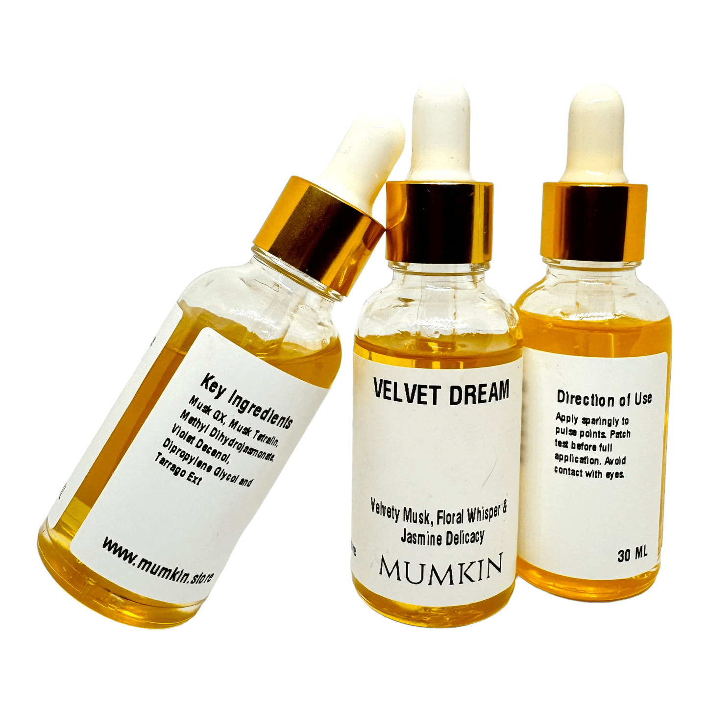 Three glass dropper bottles of 'Velvet Dream Fragrance Oil' by Mumkin, each showcasing different label details. The front label displays the product name and fragrance notes: Velvety Musk, Floral Whisper, and Jasmine Delicacy. The side labels provide key ingredients, including Musk Oil and Dipropylene Glycol, and directions for use, advising application to pulse points. Each bottle contains 30ml of golden yellow liquid and features a gold cap with a white dropper.